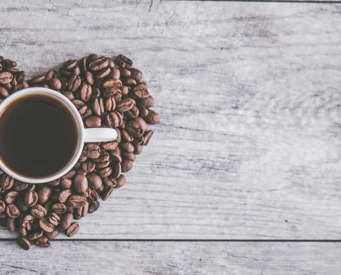 coffee beans in a heart shape with a mug of black coffee sitting on top